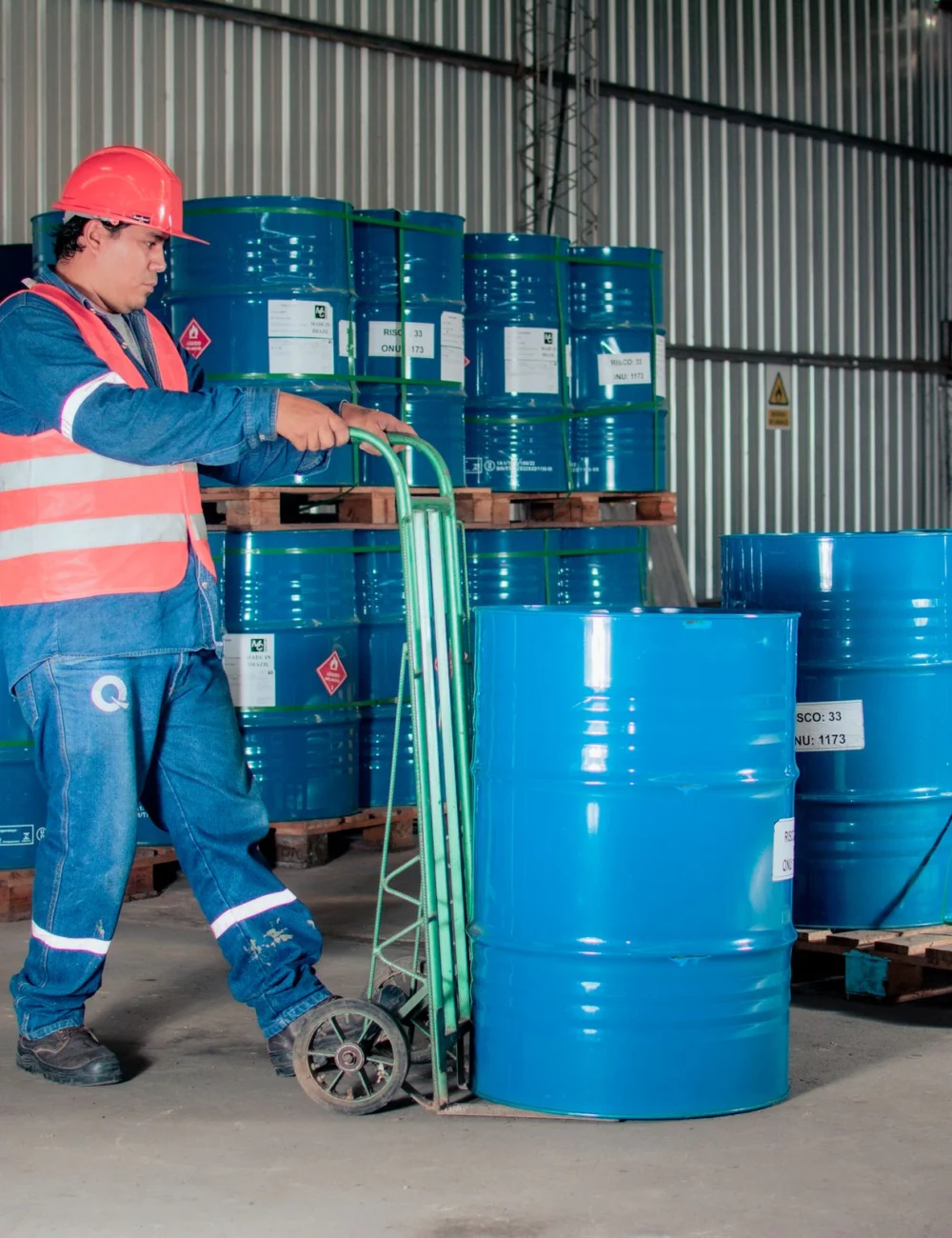 A warehouse worker in a hard hat moving blue steel drums stacked on pallets