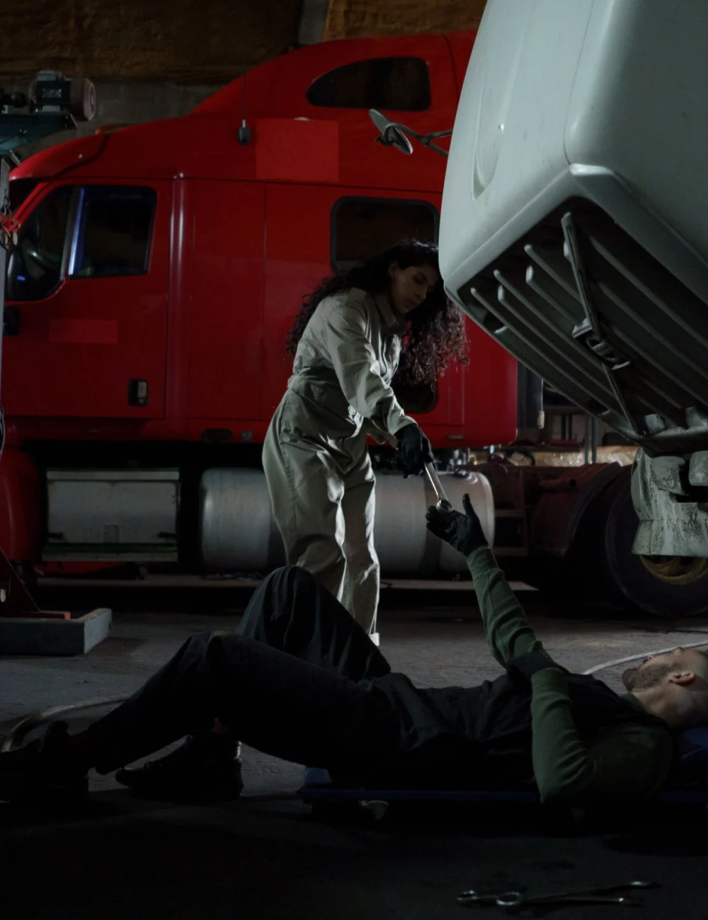 Mechanics servicing a red semi truck in a heavy-duty repair garage