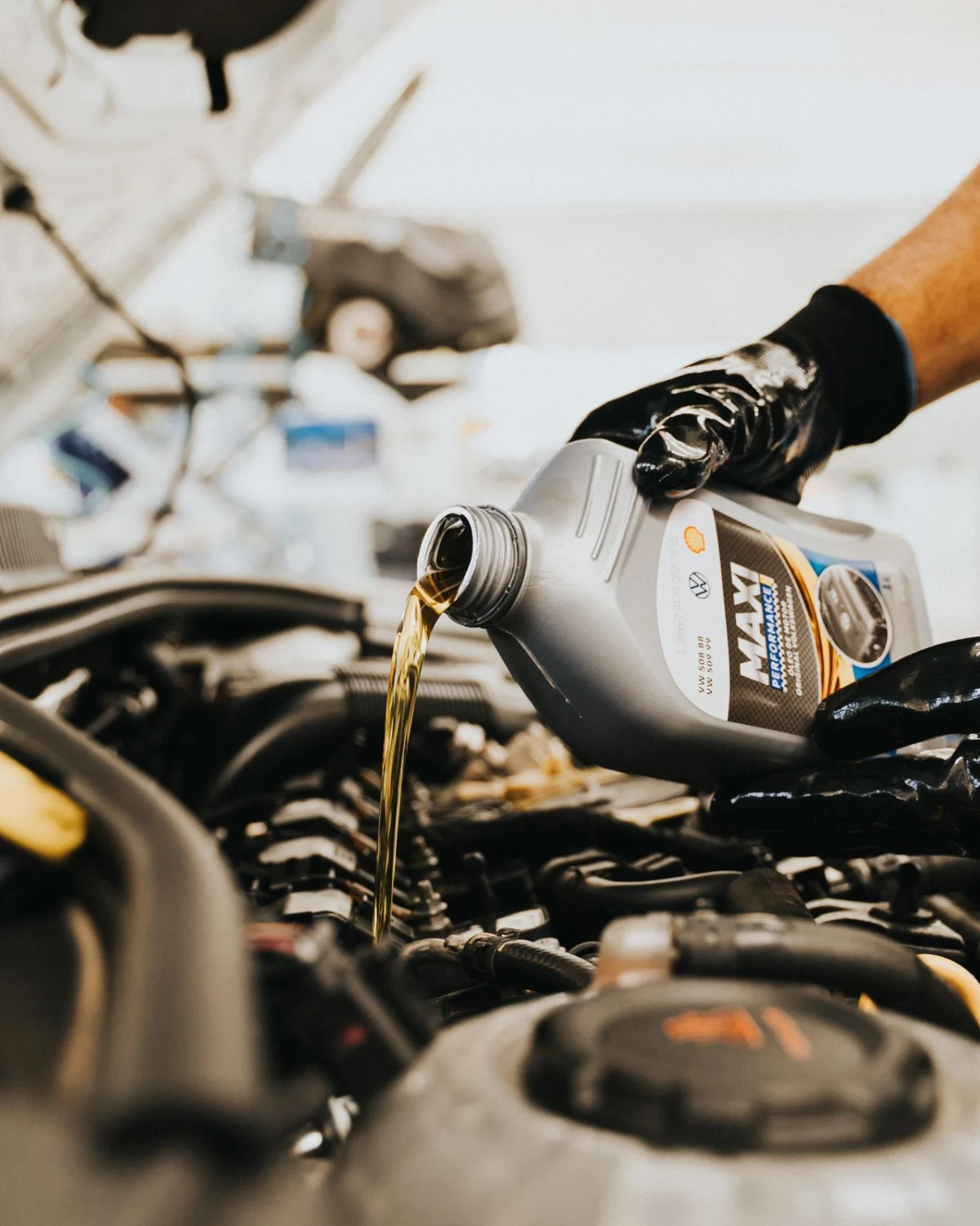 A gloved mechanic pouring automotive lubricants into a car engine during a routine oil change