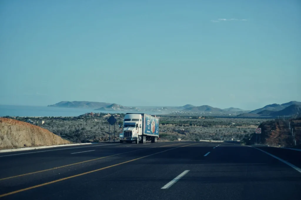 A semi truck traveling a long stretch of highway past coastal hills