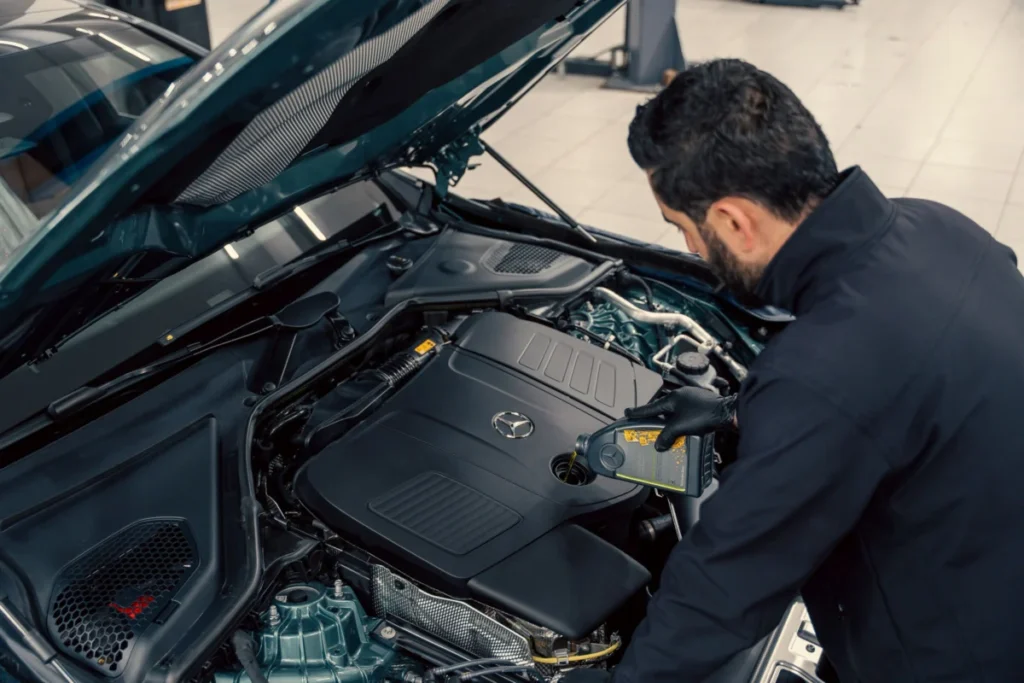 A mechanic leaning under an open hood to check a vehicle's engine oil level in a service center