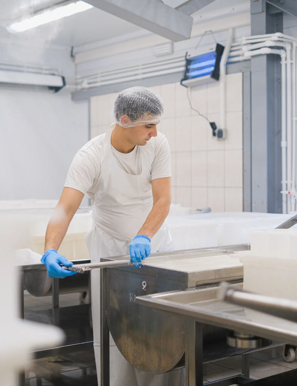 A worker in a hairnet and gloves at stainless steel equipment in a dairy processing plant, the kind of machinery food grade lubricants are made for