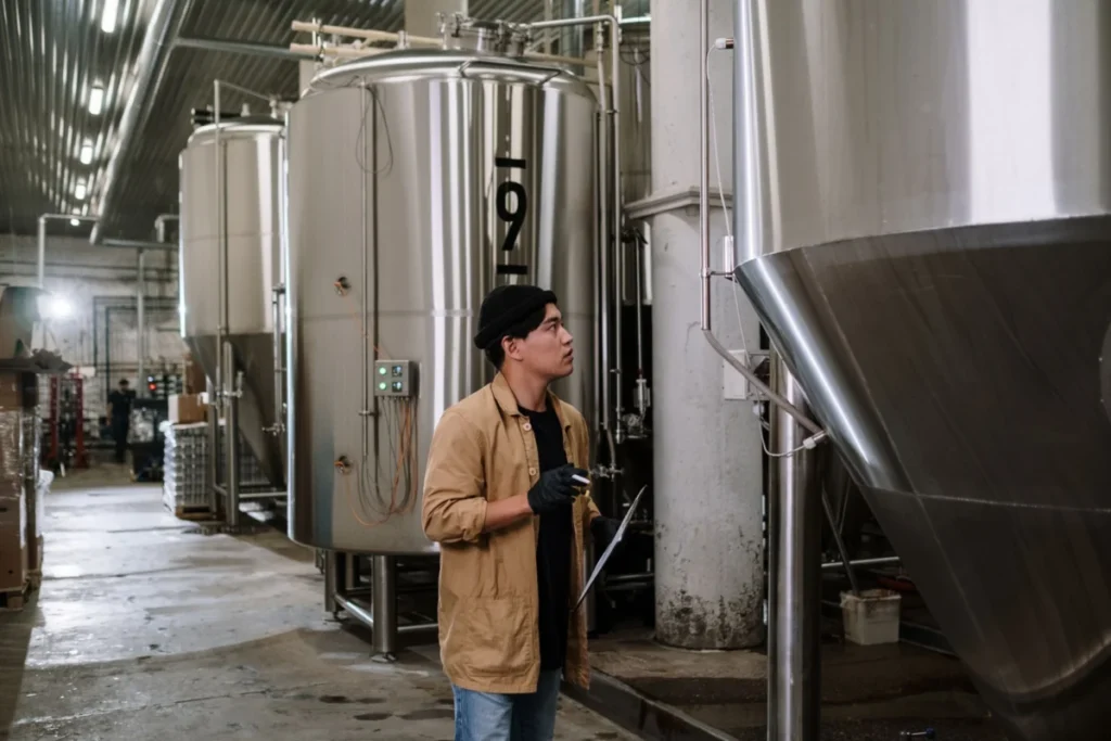 A technician checking stainless steel fermentation tanks in a beverage production facility