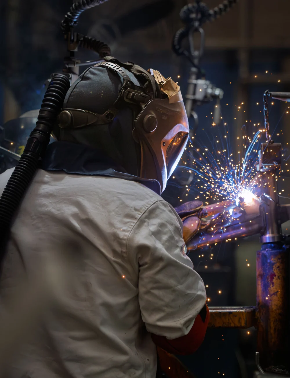 A welder in a protective helmet joining steel parts as sparks fly in a fabrication shop